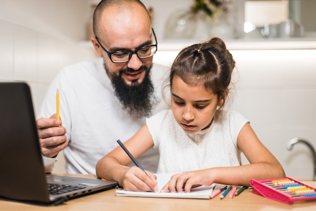 Photo père aidant sa fille à faire ses devoirs à l'aide d'un ordinateur portable numérique.