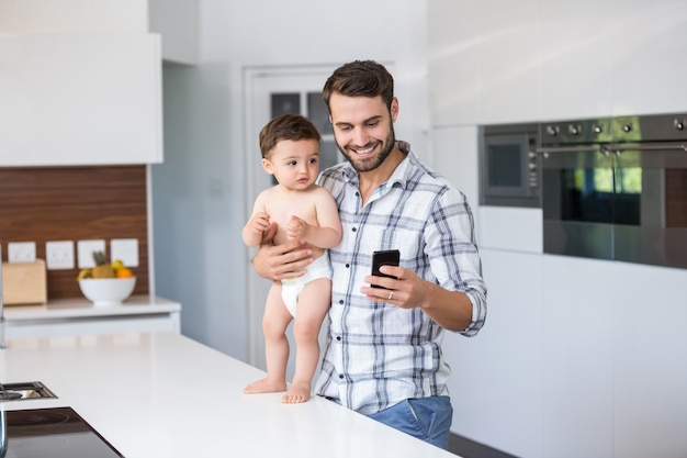 Père à l'aide de téléphone portable tout en maintenant bébé