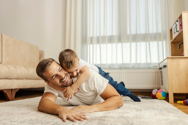 Un père aimant allongé sur le sol à la maison pendant que son fils le serre dans ses bras concept de la fête des pères