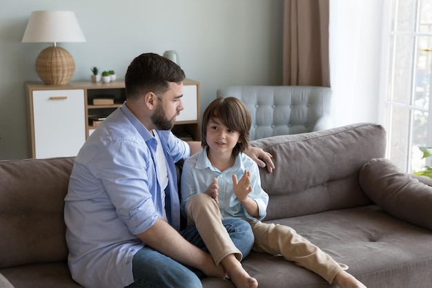 Un père aimant écoute avec intérêt son petit fils s'asseoir sur le canapé passer du temps ensemble profiter de la conversation une communication digne de confiance avoir des relations amicales chaleureuses comprendre le concept de paternité familiale
