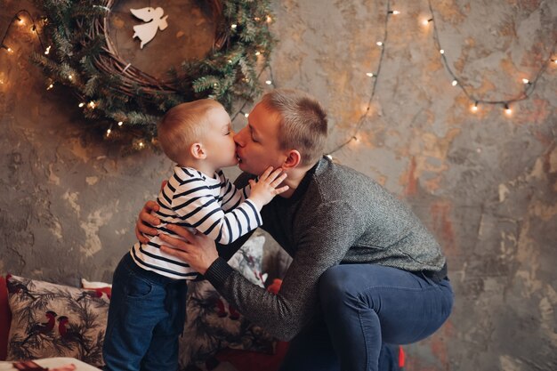 Père aimant embrassant son petit-fils et le serrant contre un mur décoré avec une guirlande et une guirlande de Noël