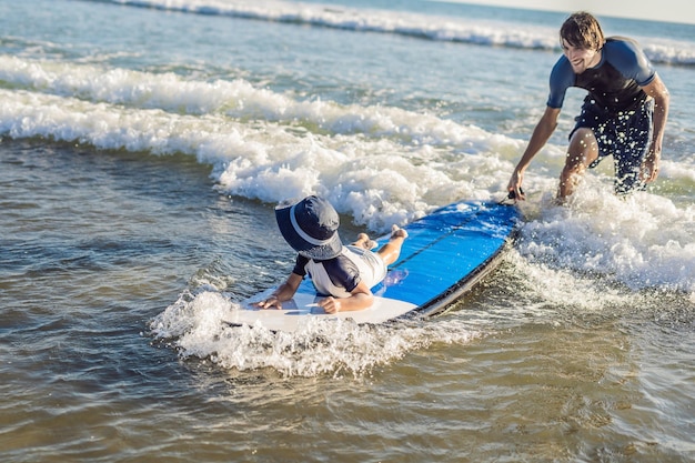 Père apprenant à son jeune fils à surfer dans la mer en vacances ou en vacances. Concept de voyage et de sport avec des enfants