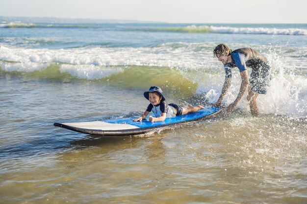 Père apprenant à son jeune fils à surfer dans la mer en vacances ou en vacances. Concept de voyage et de sport avec des enfants