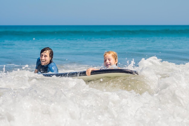 Père apprenant à son jeune fils à surfer dans la mer en vacances ou en vacances. Concept de voyage et de sport avec des enfants