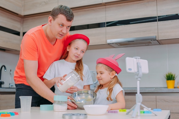 Un père apprend à deux filles à faire cuire de la pâte dans la cuisine