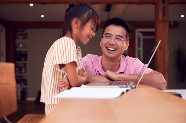 Père asiatique aidant sa fille à scolariser à la maison travaillant à table dans la cuisine sur un ordinateur portable