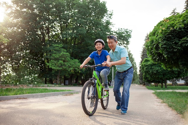 Un père asiatique apprend à son fils à faire du vélo. Un aîné coréen aide un garçon portant un casque.