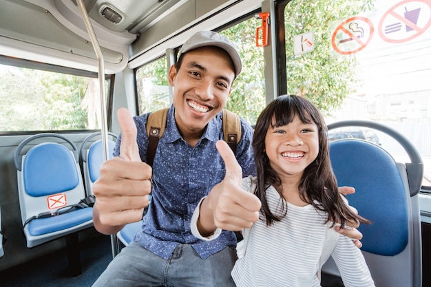 Père asiatique emmenant sa fille à l'école en bus pouce vers le haut