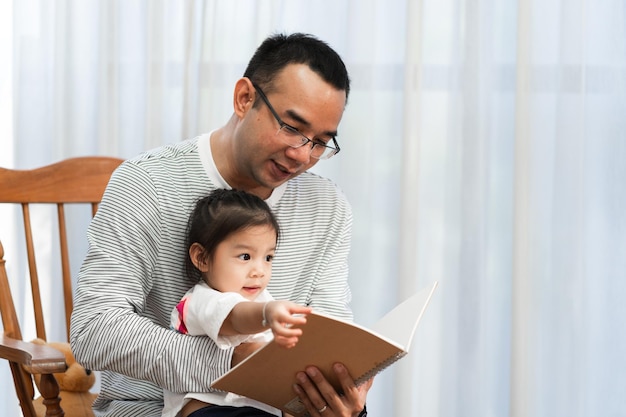 Père asiatique lisant un livre de contes à sa fille dans le salon concept de famille et développement de la petite enfance