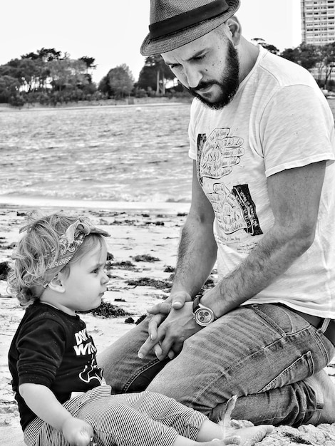 Photo un père assis avec sa fille sur la plage.