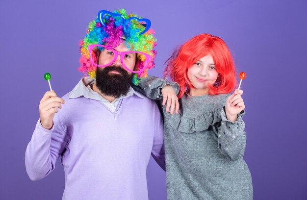 Un père barbu et une fille portent une perruque colorée tout en mangeant des bonbons à la sucette Chose que le père aimant fait pour les enfants