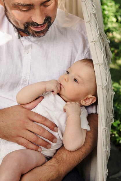 Père avec bébé garçon dans un hamac de remplissage agréable et tendre, paternité. Mignon petit fils sur les genoux de papa