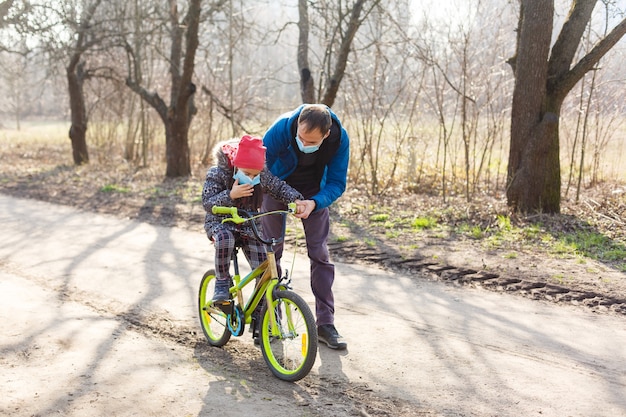 Père caucasien aidant sa fille à faire du vélo avec un masque de protection pour protéger les symptômes du virus de la pandémie de pm2.5 et du coronavirus Covid-19.