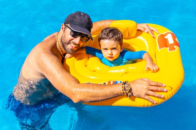 Père caucasien jouant avec son fils avec un flotteur jaune dans la piscine en été