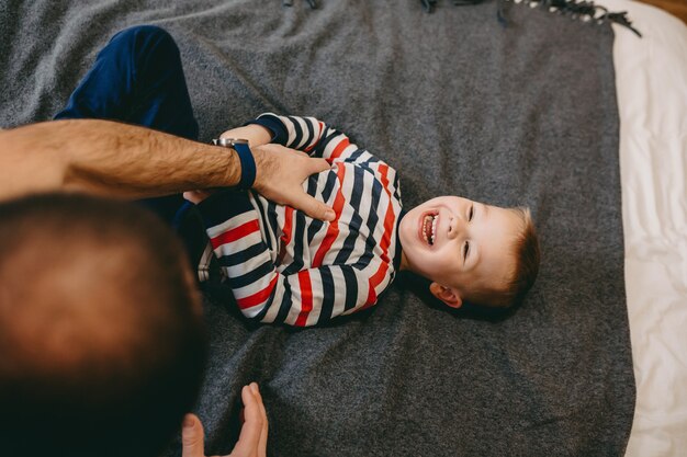 père chatouillant son fils sur le lit