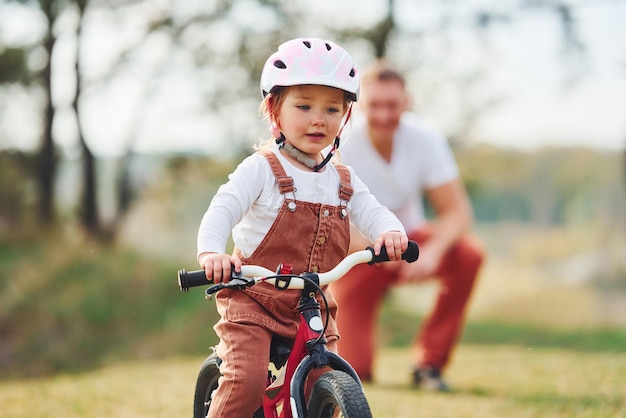 Père en chemise blanche enseignant à sa fille comment faire du vélo à l'extérieur