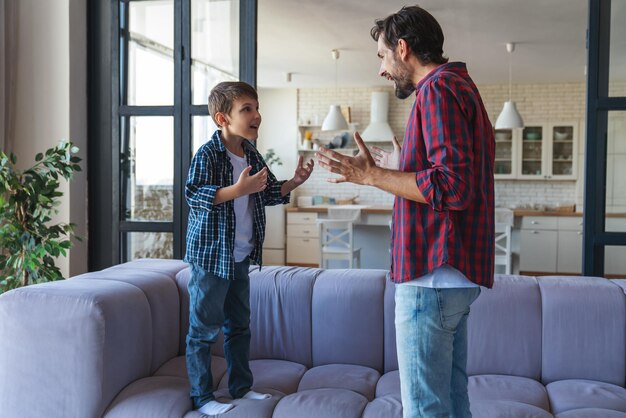 Un père en colère et son petit fils se disputent et s'expliquent quelque chose à la maison dans le salon.