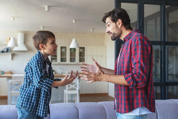 Un père en colère et son petit fils se disputent et s'expliquent quelque chose à la maison dans le salon.