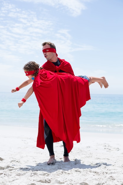 Père en costume de super-héros fils de levage au bord de mer