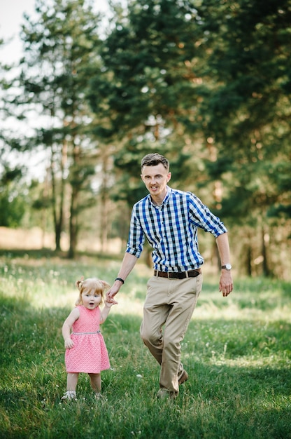 Le père court avec une fille et lui tient la main sur la nature pendant les vacances d'été. Papa et fille marchant et jouant dans le parc à l'heure du coucher du soleil. Concept de famille sympathique. Fermer.