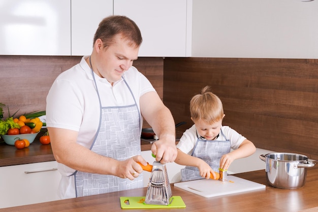 Le père cuisine avec son fils frotter les carottes sur la râpe à la maison dans la cuisine