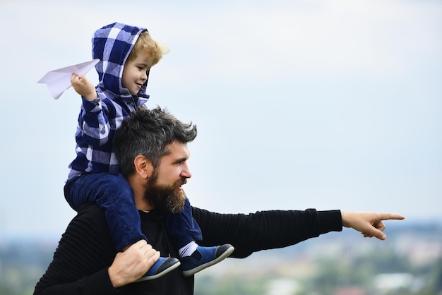 Père donnant son tour à son fils dans le parc père et fils construisant ensemble un avion en papier enfant heureux