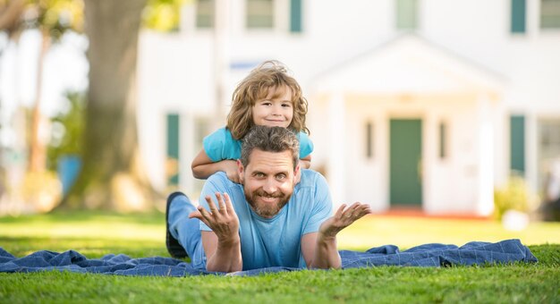 Un père drôle avec son fils se détend ensemble sur l'herbe du parc verdoyant, l'amitié.