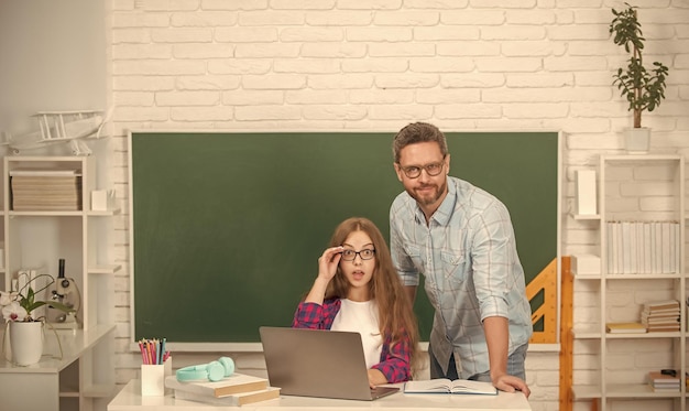 Un père et un enfant étonnés étudient à l'école avec un ordinateur portable sur fond de tableau noir