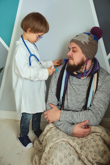 Père et enfant jouant à la clinique et médecin petit garçon en blouse médicale avec stéthoscope traite papa