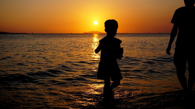 Père et enfant jouant sur la plage à l'heure du coucher du soleil. Concept de famille sympathique.