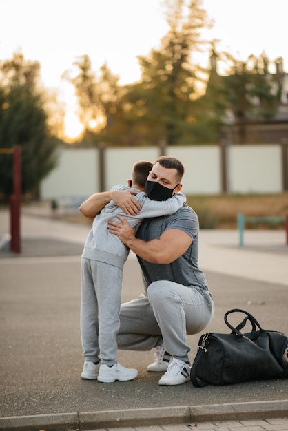 Le père et l'enfant se tiennent sur le terrain de sport dans des masques après l'entraînement au coucher du soleil