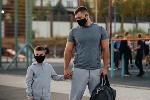 Un père et un enfant se tiennent sur un terrain de sport masqués après un entraînement au coucher du soleil.