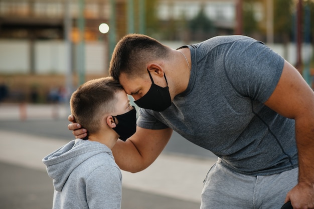 Un père et un enfant se tiennent sur un terrain de sport avec des masques après s'être entraînés au coucher du soleil.