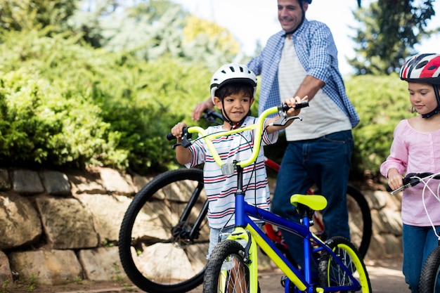 Photo père et enfants debout avec vélo dans le parc