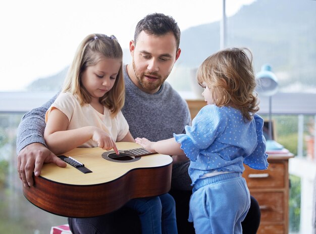 Le père et les enfants et la guitare à la maison pour apprendre la musique et la créativité ou l'éducation ensemble Les enfants de la famille et le père ou l'homme dans le salon pour le développement de l'enseignement et du talent pour l'écoute dans le salon