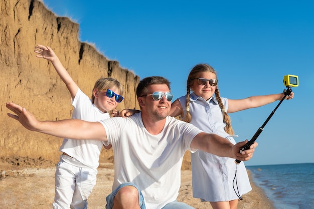 Père avec enfants prenant selfie sur la plage pendant la journée.