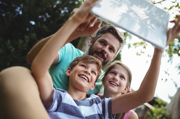 Père et enfants prenant un selfie avec tablette numérique