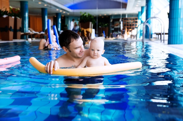 Père enseignant à bébé à nager enfant de 11 mois en classe dans une piscine Vie de famille saine