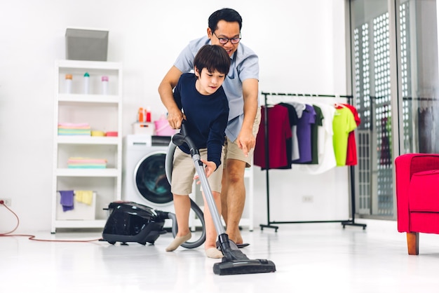 Père enseignant enfant asiatique petit garçon fils s'amusant à faire les tâches ménagères, nettoyer et laver le sol en essuyant la poussière avec un aspirateur tout en nettoyant la maison ensemble à la maison.