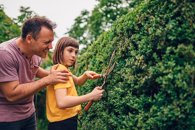 Père enseignant fille à élaguer la haie