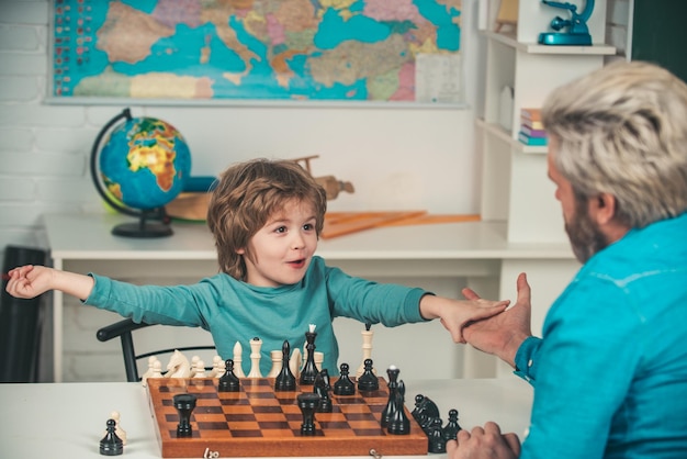 Père enseignant son fils Heureux petit enfant jouant aux échecs avec un homme âgé à la maison Heureux deux générations d'hommes s'amusent et jouent aux échecs