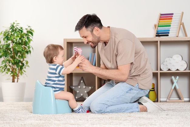 Père entraînant son enfant à s'asseoir sur un pot de bébé à l'intérieur