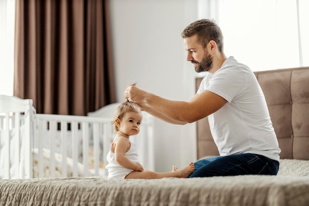 Un père fait une coiffure sur la tête de sa fille dans une chambre