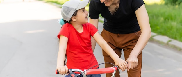 Photo un père de famille heureux apprend à sa fille à faire du vélo dans le parc dans la nature.