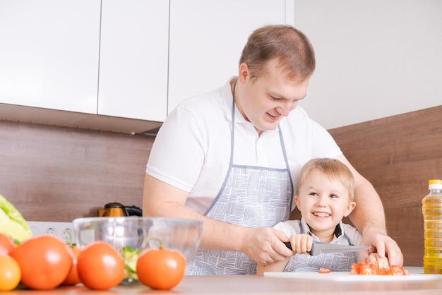 Père de famille heureux avec son fils préparant une salade de légumes à la maison