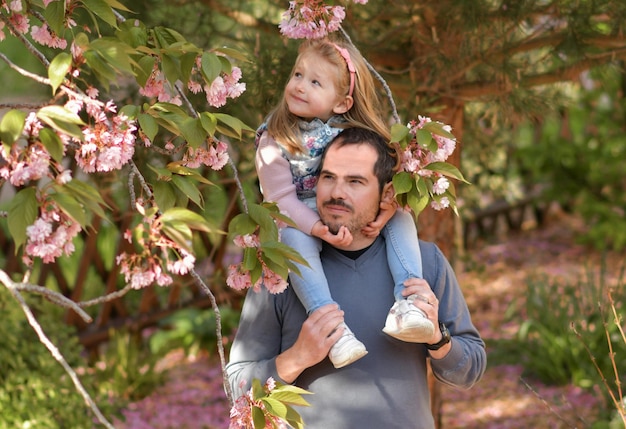 Photo père et fille dans un jardin fleuri avec un sakura rose