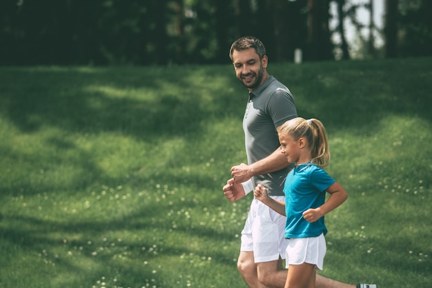 Père et fille faisant du jogging. Vue latérale d'un père et d'une fille joyeux faisant du jogging ensemble dans un parc