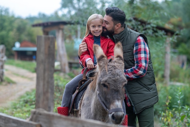 Père et fille à la ferme d'élevage avec un âne