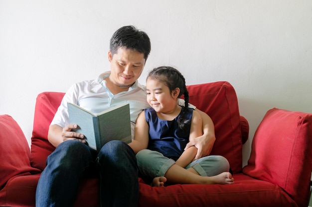 Père et fille lisent des livresAssis sur un canapé rougeC'est une bonne pratique d'apprentissage et une bonne relation familialela lumière brilleComme de nouvelles choses De bonnes choses arrivent