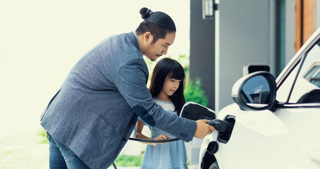 Un père et une fille progressistes chargeant une voiture électrique à partir d'une station de charge à domicile